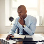 gestão empresarial - homem de camisa social e gravata em sentado um escritório com uma postura pensativa observando dados em um notebook