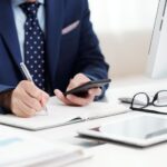 momento certo para trocar de sistema ERP - homem em uma mesa de escritório escrevendo e usando o celular