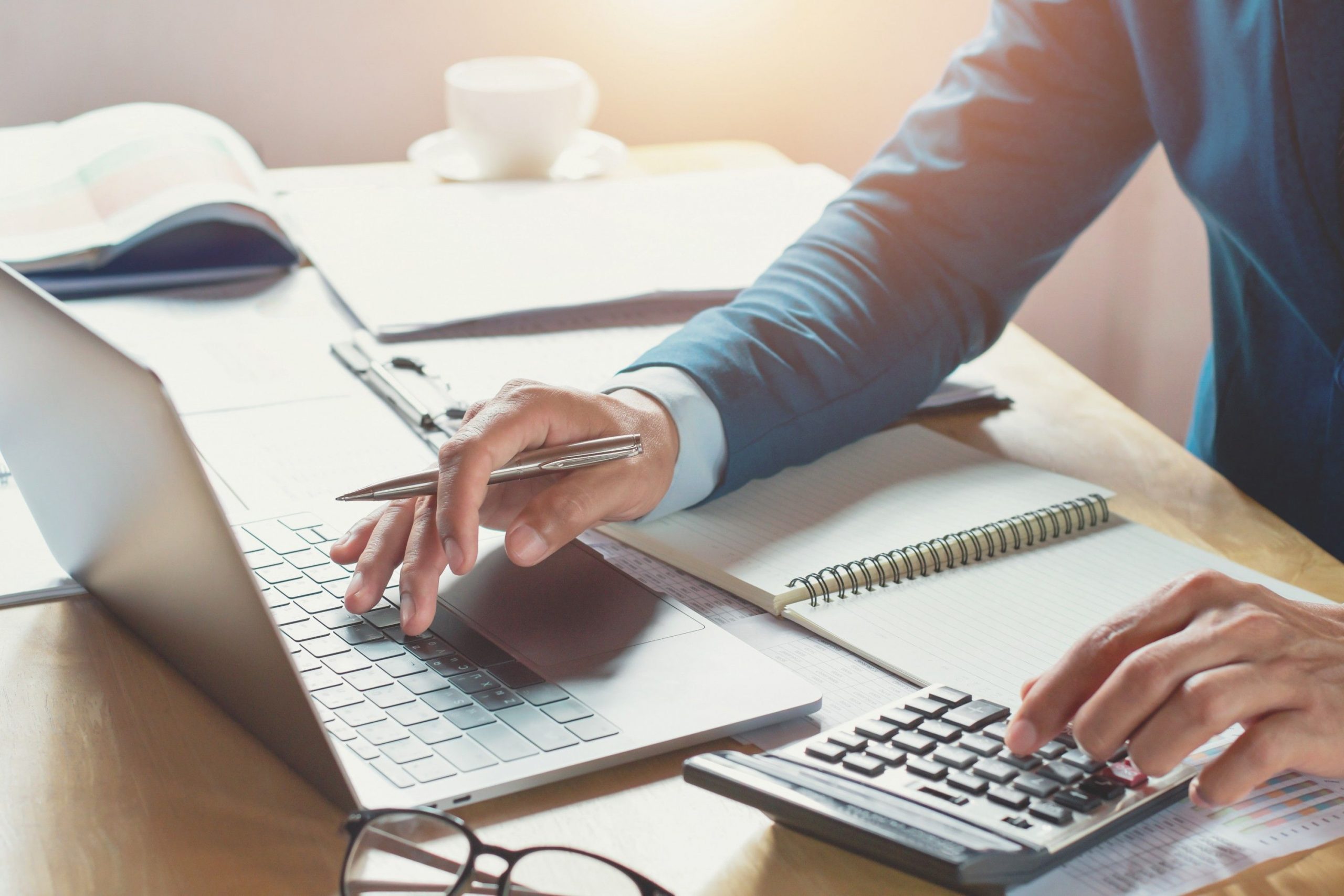 custeio por absorção - homem utilizando notebook e fazendo contas com uma calculadora em uma mesa de escritório