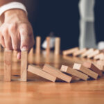supply chain - imagem com dominós em queda e uma mão segurando os demais da fila para que não caiam