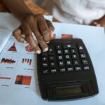 gestão financeira - pessoa utilizando calculadora em uma mesa com papéis contendo gráficos e dados financeiros