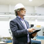 lean manufacturing - homem com terno e capacete utilizando tablet numa indústria