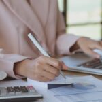 amortização - mulher avaliando dados financeiros em papéis e notebook com uma calculadora ao lado