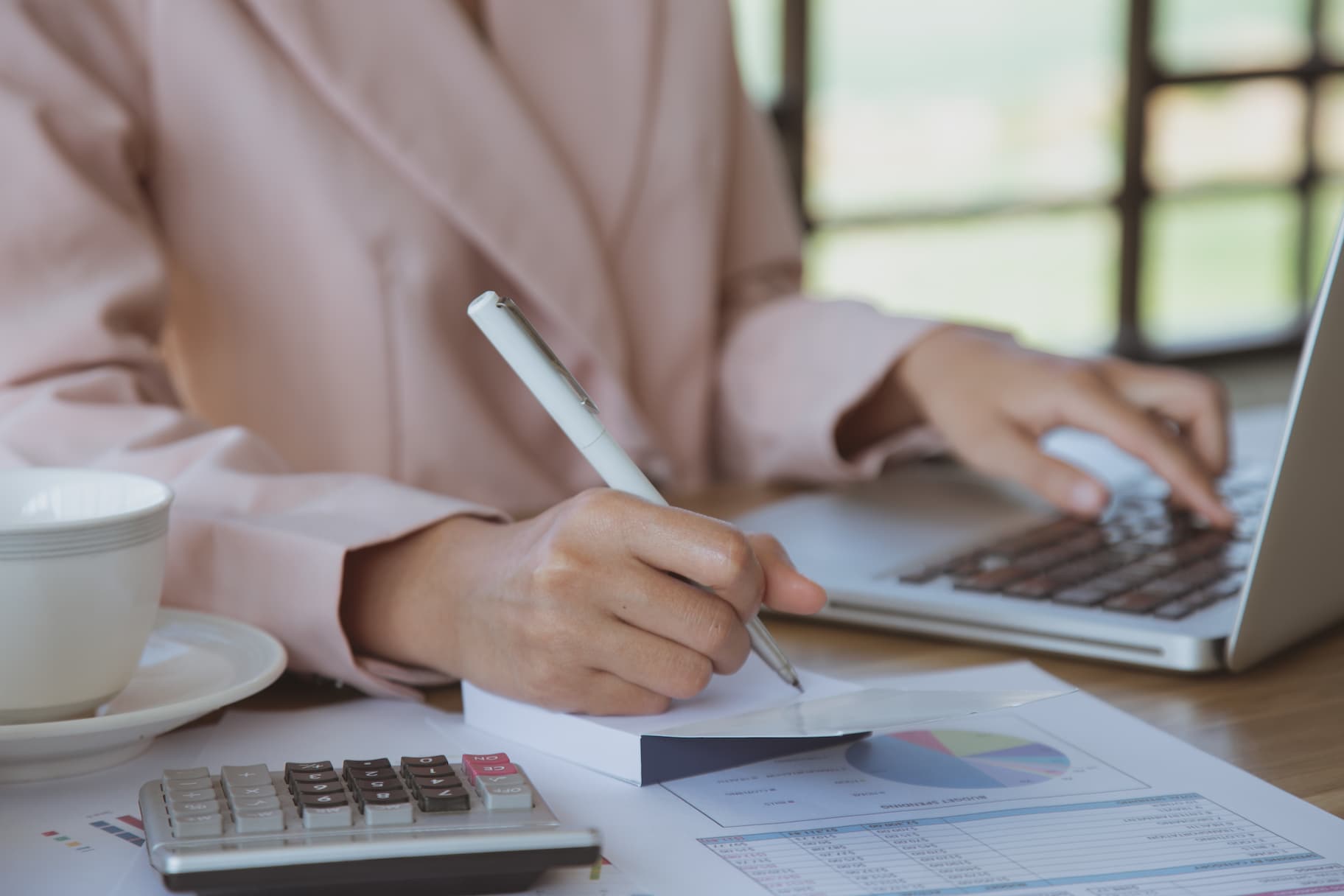 amortização - mulher avaliando dados financeiros em papéis e notebook com uma calculadora ao lado