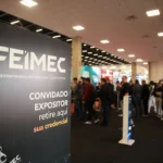 FEIMEC 2024 - Imagem com o banner da feira e ao fundo pessoas na fila da retirada de credenciais