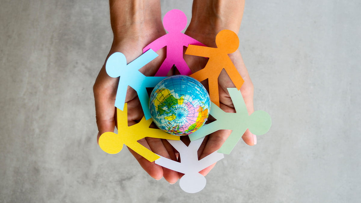 responsabilidade social - pessoa segurando miniatura do globo com recortes de pessoas ao redor do globo de braços dados