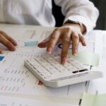 planejamento financeiro - mulher utilizando calculadora sobre uma mesa com várias folhas contendo dados e gráficos impressos