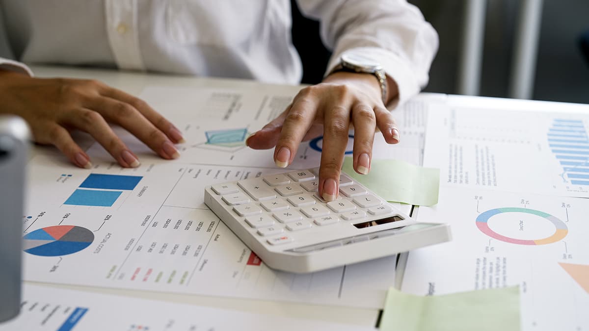 planejamento financeiro - mulher utilizando calculadora sobre uma mesa com várias folhas contendo dados e gráficos impressos