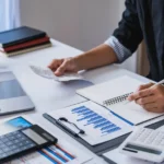 ISSQN - pessoa em um escritório avaliando gráficos e informações em um notebook e papéis impressos