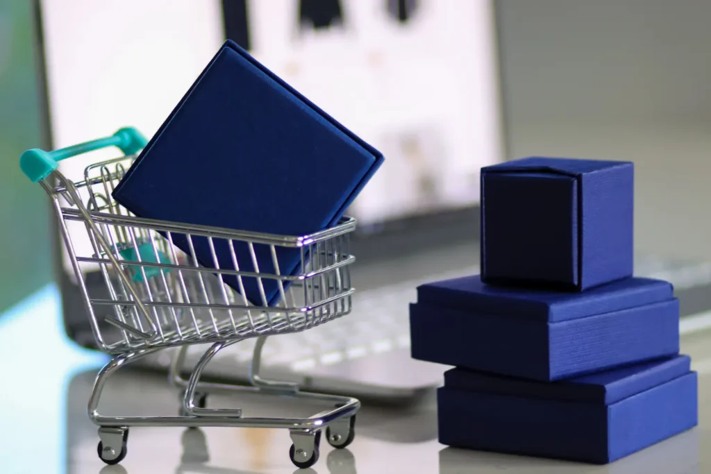marketplace o que é - carrinho de compras miniatura com caixa azul dentro dele enquanto outras caixas estão empilhadas ao lado